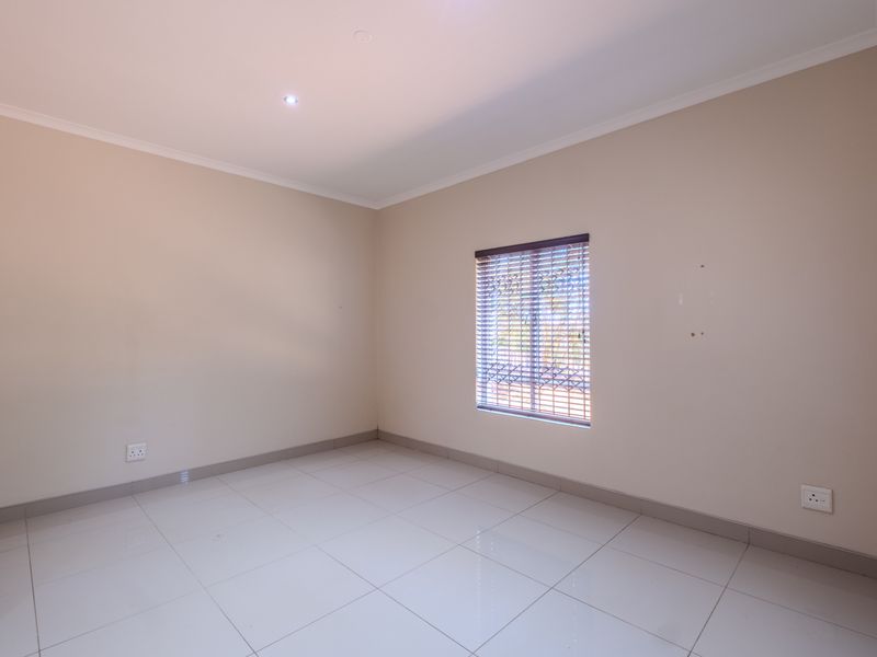 A bright, empty bedroom featuring neutral tiled flooring, recessed lighting, and venetian blinds, providing a clean canvas for personalization.