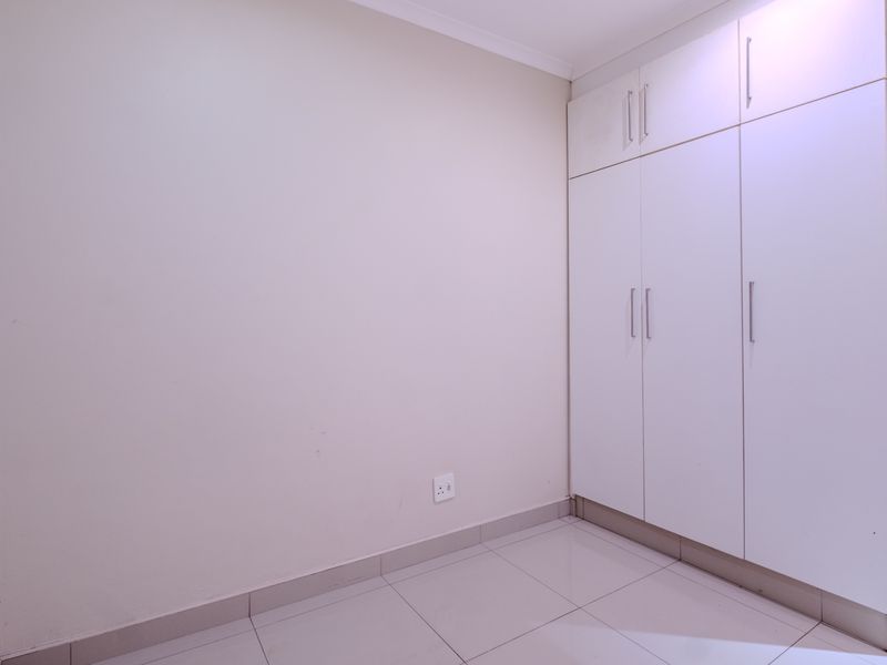 A clean, empty bedroom featuring neutral tiled flooring and ample built-in cupboard storage space.