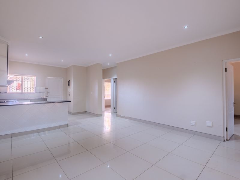 Spacious open-plan living area featuring neutral tiled flooring, recessed lighting, and a functional kitchen with a breakfast bar and built-in cabinetry.