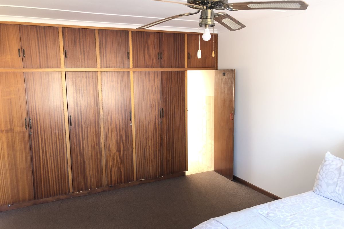 A bedroom featuring extensive floor-to-ceiling built-in wooden cupboards, a ceiling fan, and carpeted flooring.