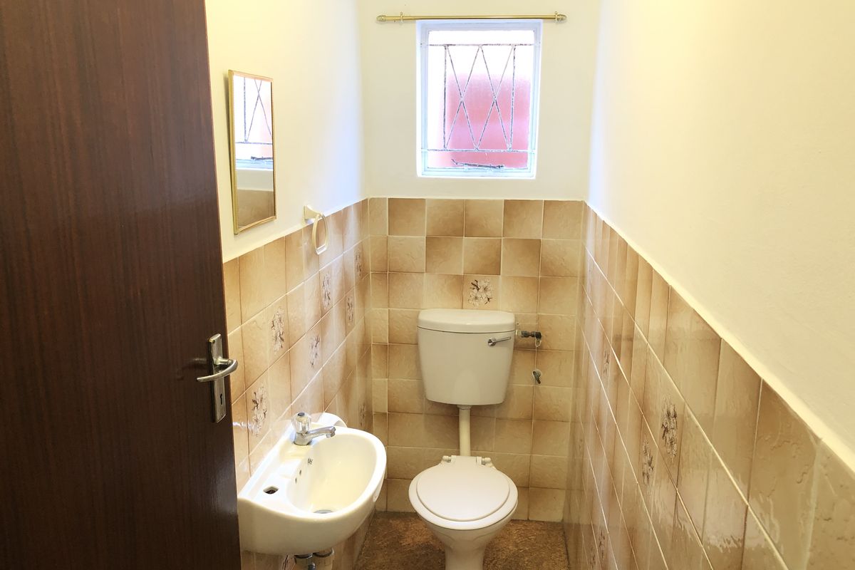 A compact guest bathroom featuring dated ceramic wall tiles, a pedestal basin, and a toilet with a leaded glass window.