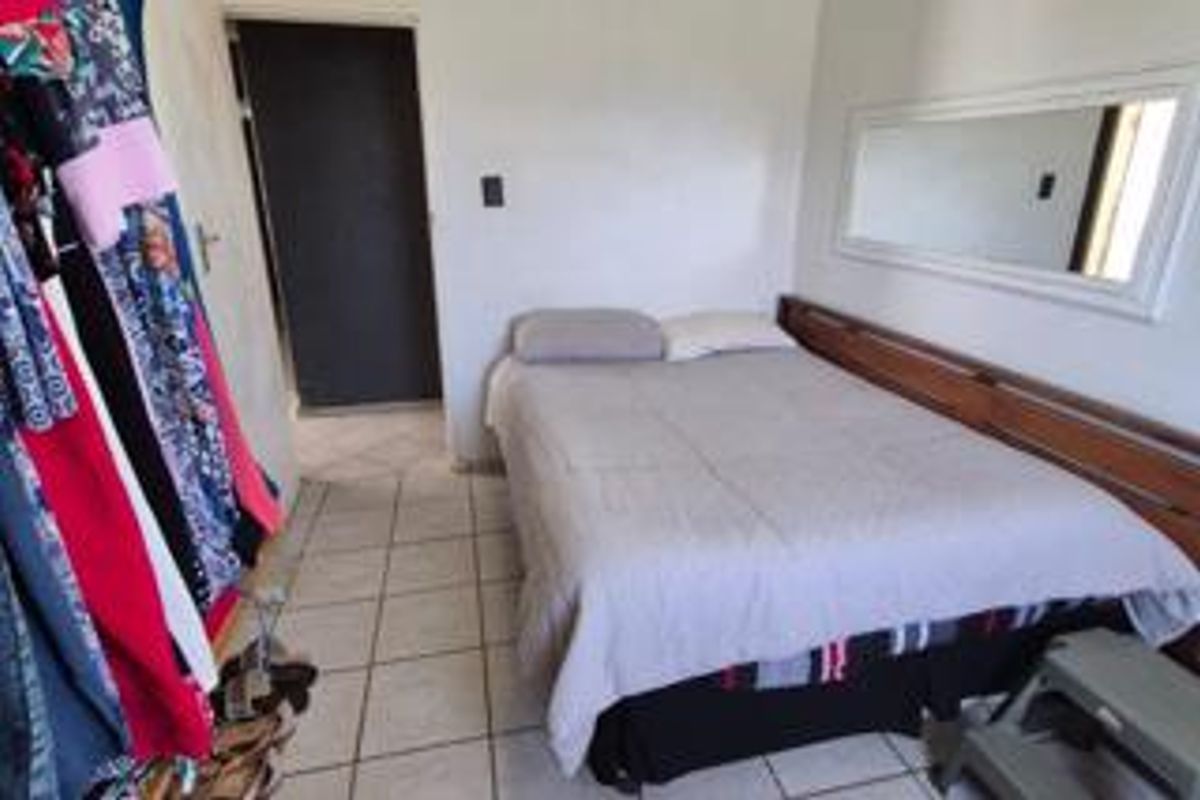A functional bedroom featuring tiled flooring and a built-in wooden headboard, providing a simple and practical sleeping space.