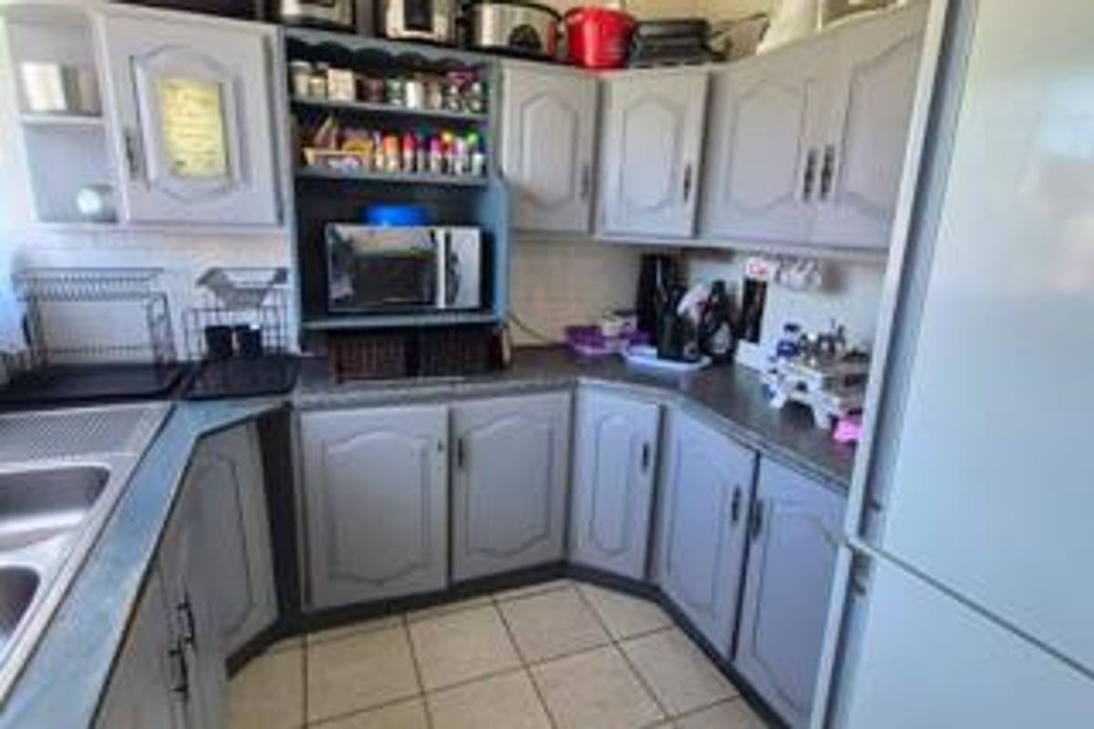 A functional kitchen featuring grey cabinetry, laminate countertops, and tiled flooring, offering a practical layout with ample storage space.