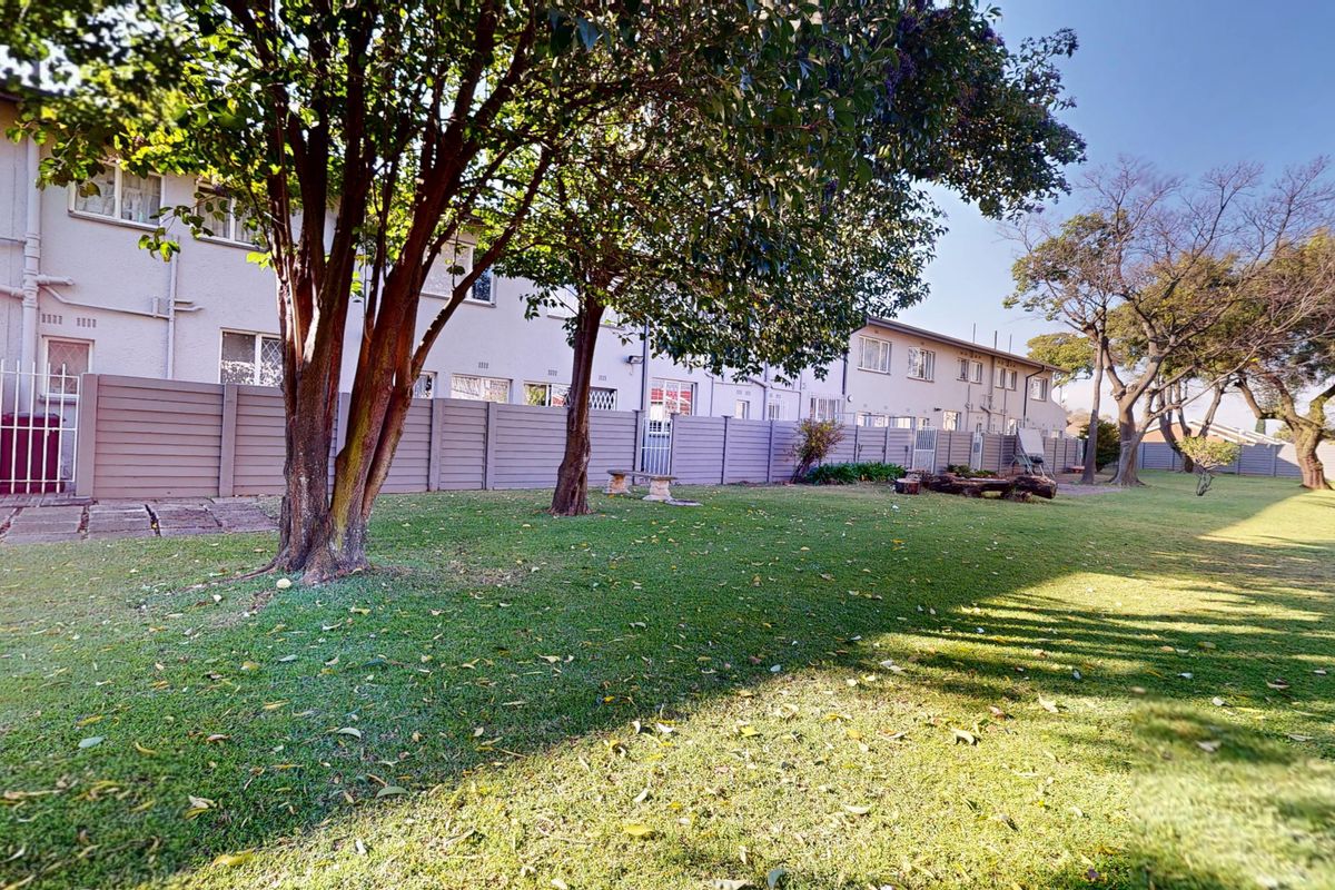 Spacious rear garden area featuring a well-maintained lawn, mature trees, and a secure precast concrete boundary wall.