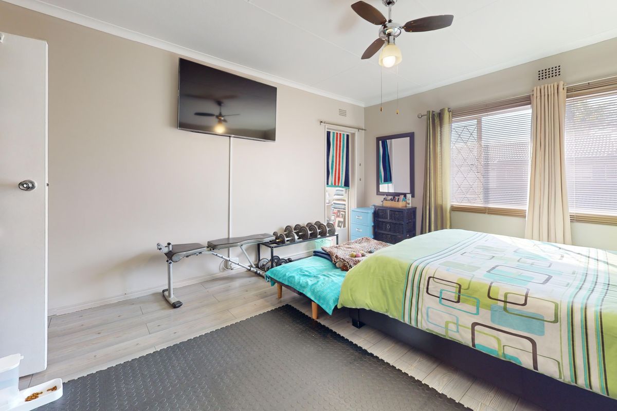 A bedroom featuring laminate flooring, a ceiling fan, and built-in storage, currently utilized as a multi-purpose living and exercise space.