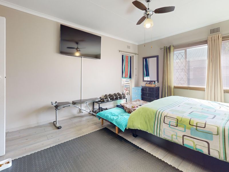 A bedroom featuring laminate flooring, a ceiling fan, and built-in storage, currently utilized as a multi-purpose living and exercise space.