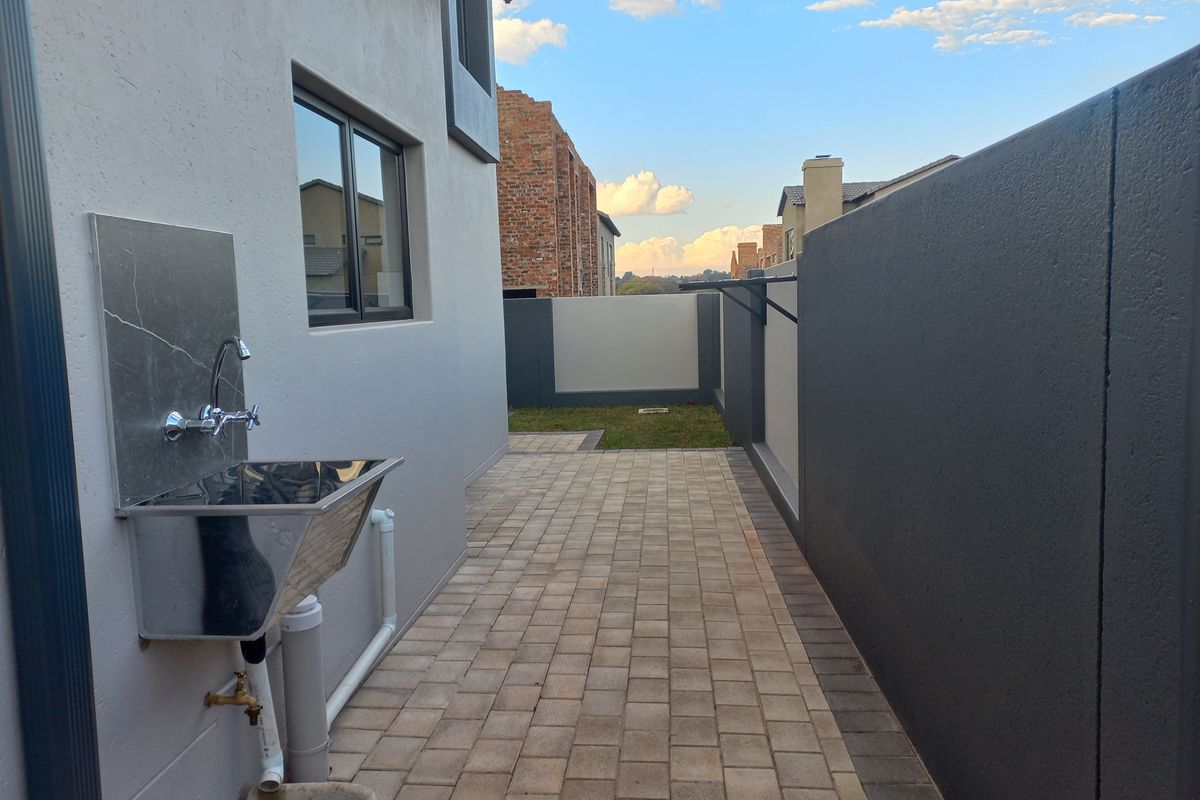 A clean, paved rear exterior area featuring a stainless steel utility sink, external tap, and secure boundary walls.