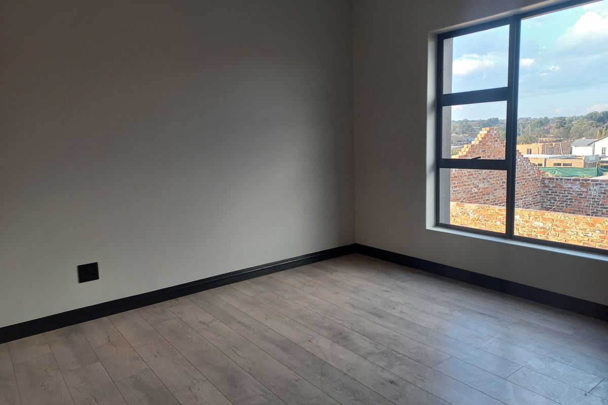 A bright, empty bedroom featuring modern laminate flooring, black skirting boards, and a large window with views of the surrounding neighborhood.