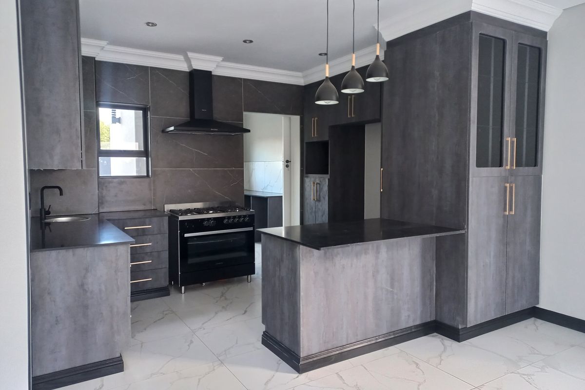 Modern kitchen featuring dark grey cabinetry, stone countertops, a gas stove with extractor fan, and a central island with pendant lighting.