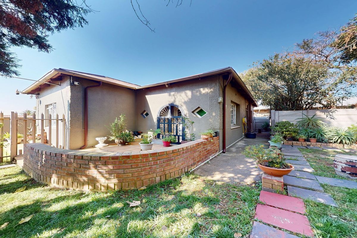 Rear exterior view of the house featuring a paved patio area, brick retaining wall, and established garden space with boundary walling.