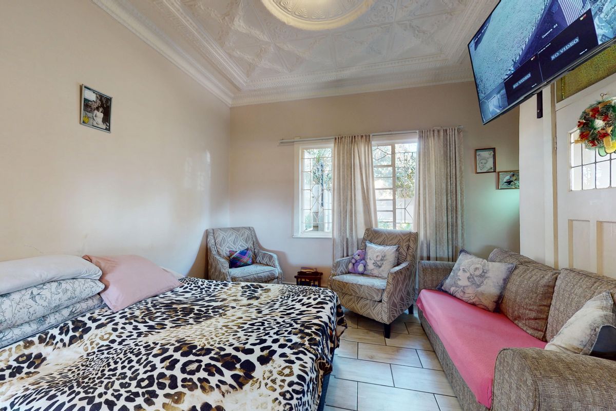 A bedroom featuring a decorative plaster ceiling with a central rose, tiled flooring, and a leaded glass window.
