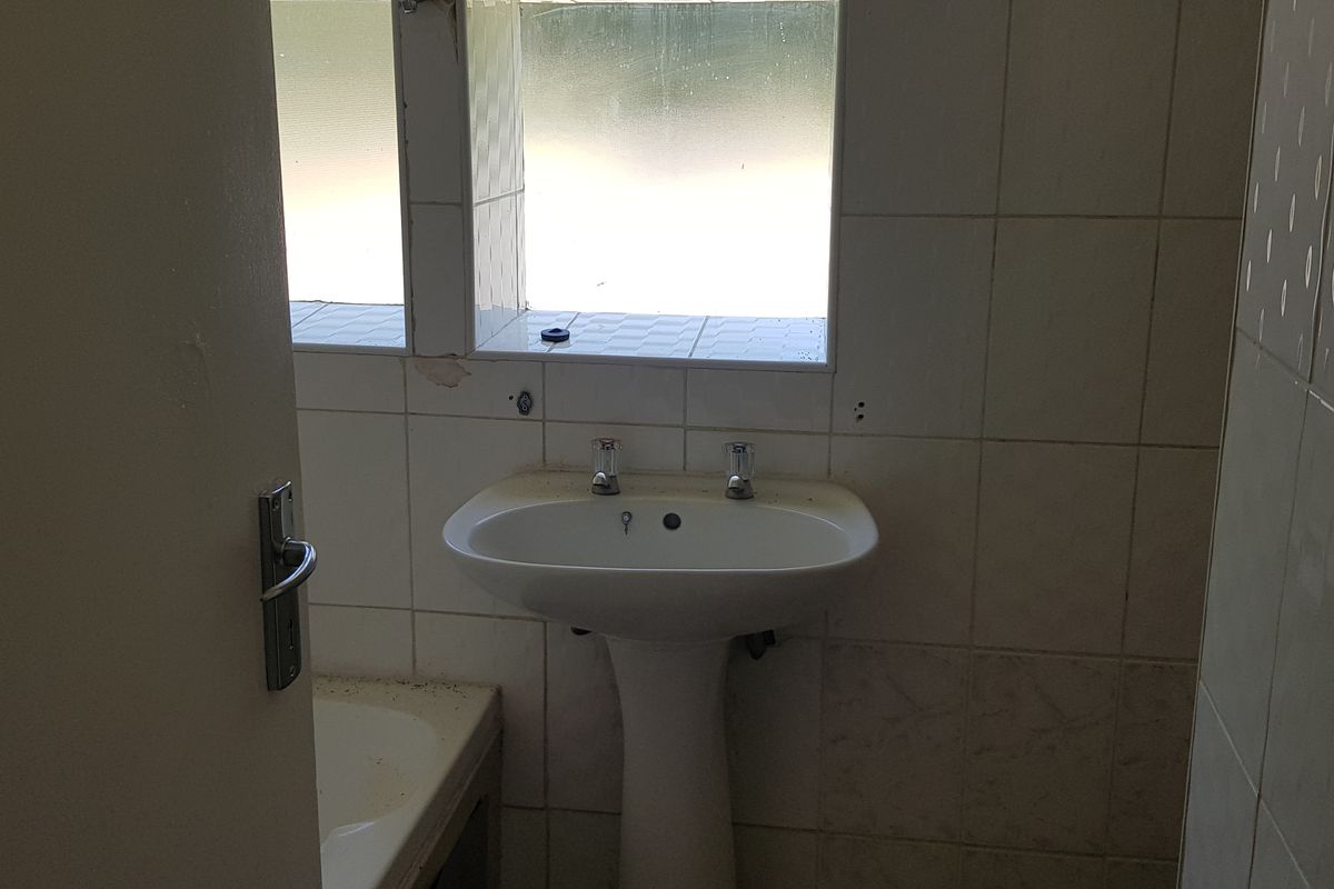 A dated bathroom featuring a pedestal basin and tiled walls, requiring cosmetic updates and maintenance to restore its functionality and appeal.