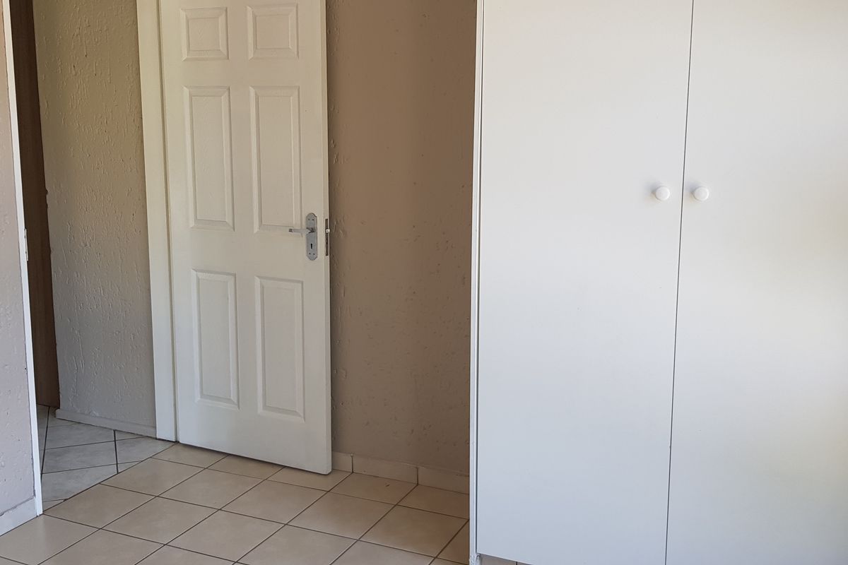 A bedroom interior featuring built-in cupboards, tiled flooring, and a standard door, providing a functional and neutral living space.