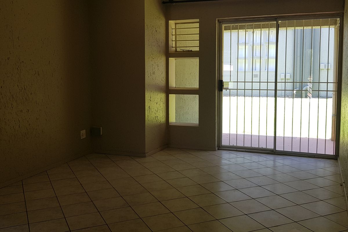 An empty living area featuring tiled flooring, textured walls, and a sliding glass door with security bars leading to the exterior.