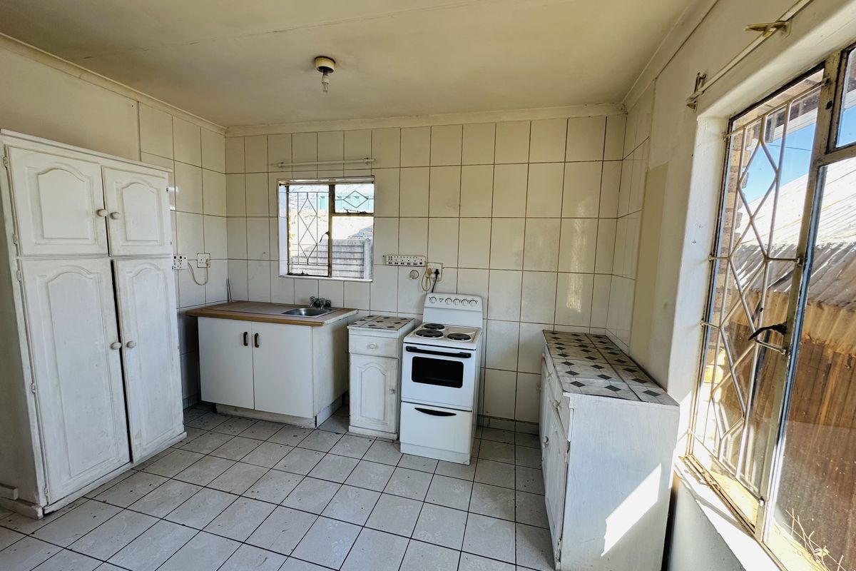 A dated kitchen featuring tiled splashbacks, built-in cabinetry, and a freestanding electric stove, offering significant potential for modernization and renovation.