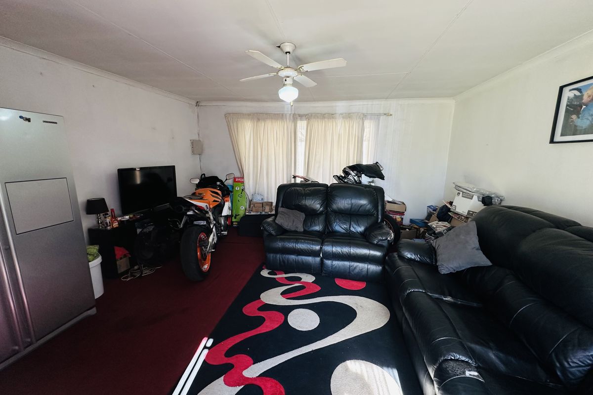 A living room space featuring a ceiling fan and carpeted flooring, currently utilized for storage and living purposes.
