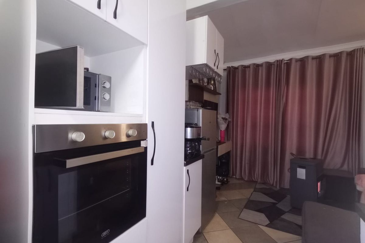 A functional kitchen area featuring white built-in cabinetry, a modern oven, and tiled flooring, leading into an adjacent living space.
