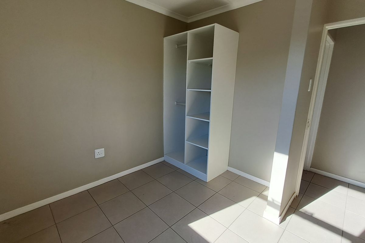 A clean, empty bedroom featuring neutral wall tones, tiled flooring, and a built-in white shelving unit for storage.