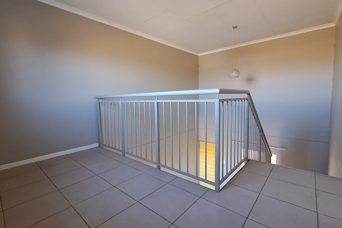 A spacious upper-level landing area featuring neutral tiled flooring and a secure metal balustrade overlooking the staircase.