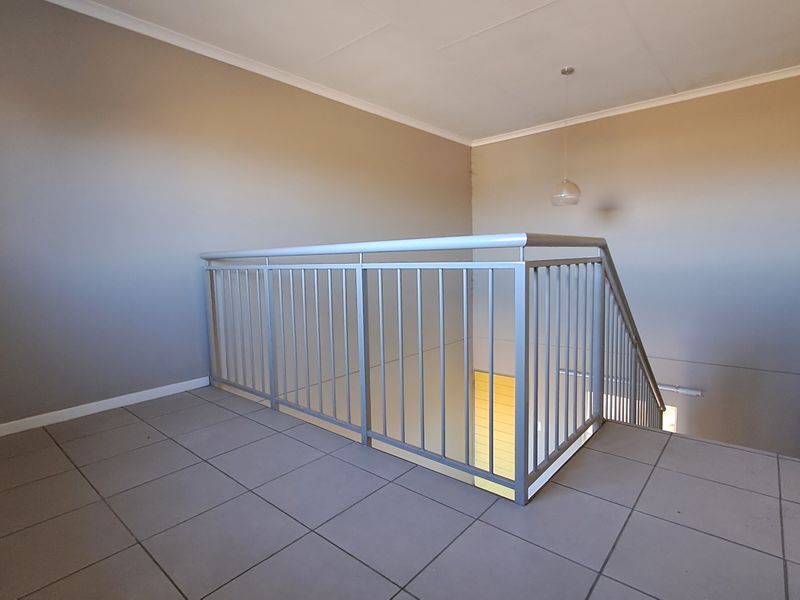 A spacious upper-level landing area featuring neutral tiled flooring and a secure metal balustrade overlooking the staircase.