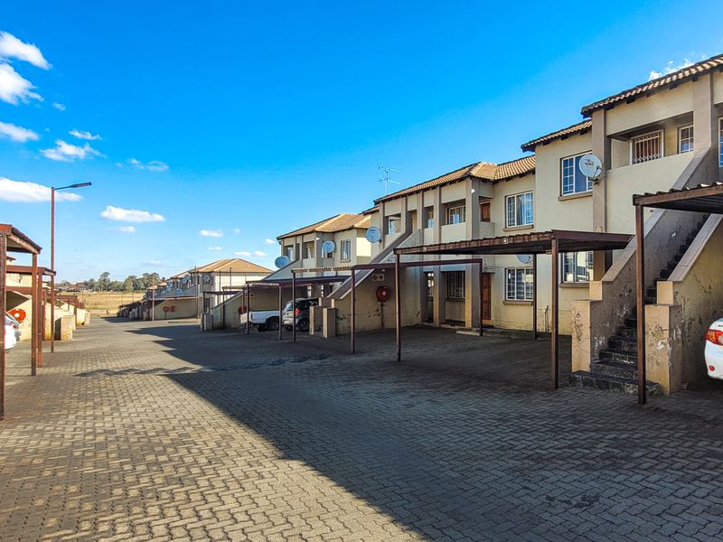 Exterior view of an apartment complex featuring paved parking areas, covered carports, and external staircases leading to upper-level units.