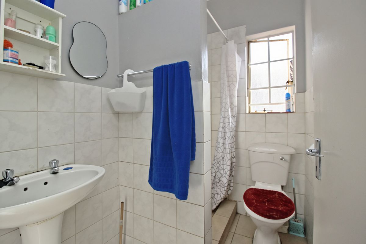 A functional bathroom featuring a pedestal basin, toilet, and a shower area with tiled walls and flooring.