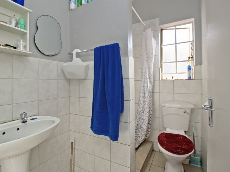 A functional bathroom featuring a pedestal basin, toilet, and a shower area with tiled walls and flooring.