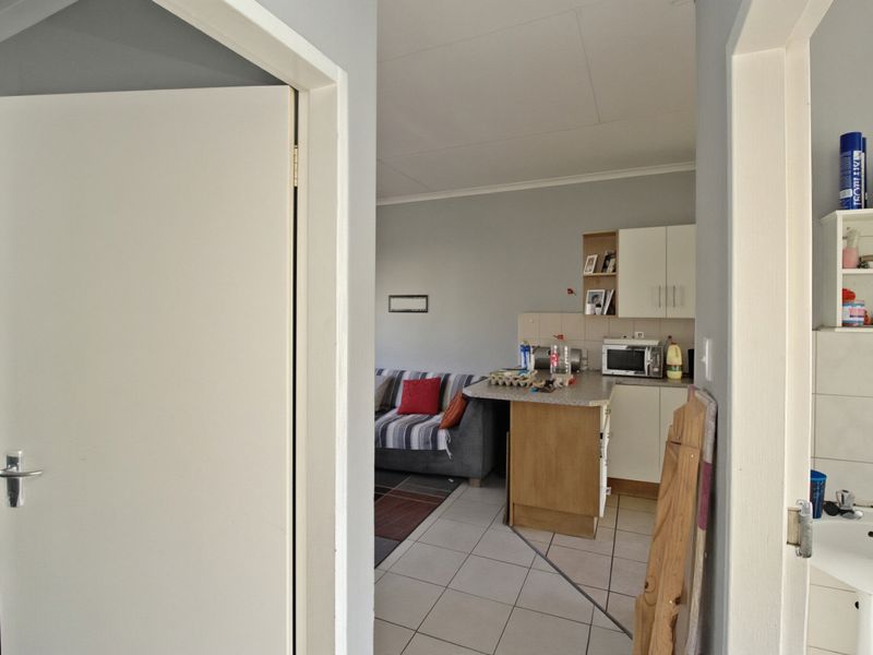 Open-plan living and kitchen area featuring tiled flooring, functional cabinetry, and a breakfast counter, viewed through an interior doorway.