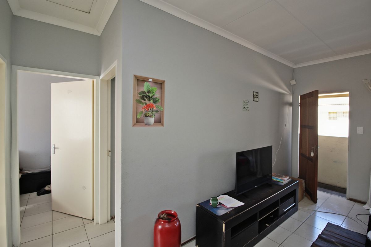 A living area featuring neutral grey walls, tiled flooring, and coved ceiling cornices, providing access to adjacent rooms and an exterior doorway.