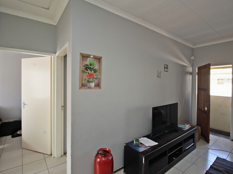 A living area featuring neutral grey walls, tiled flooring, and coved ceiling cornices, providing access to adjacent rooms and an exterior doorway.