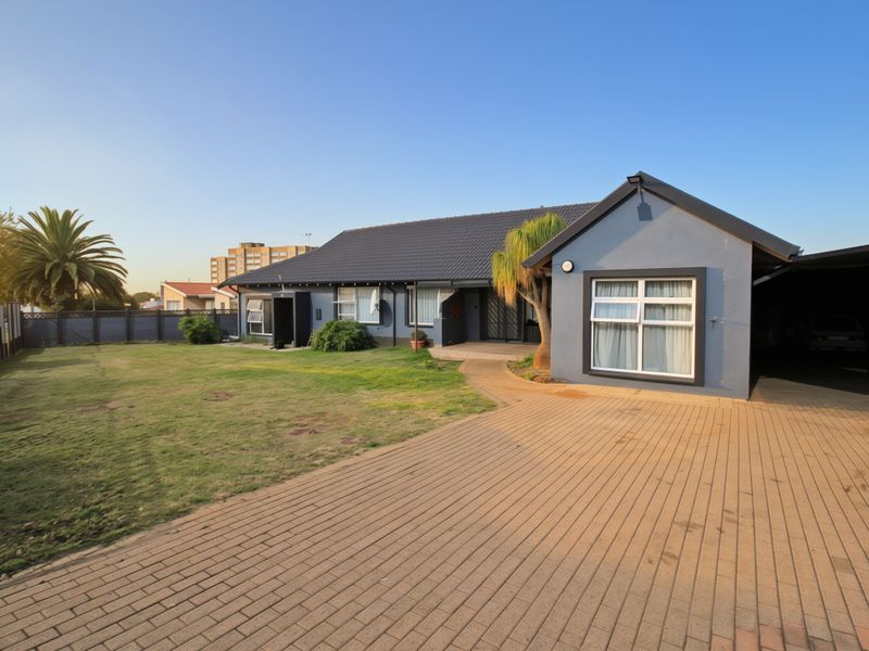 A well-maintained single-story house featuring a paved driveway, carport, and a spacious front lawn with modern exterior finishes.