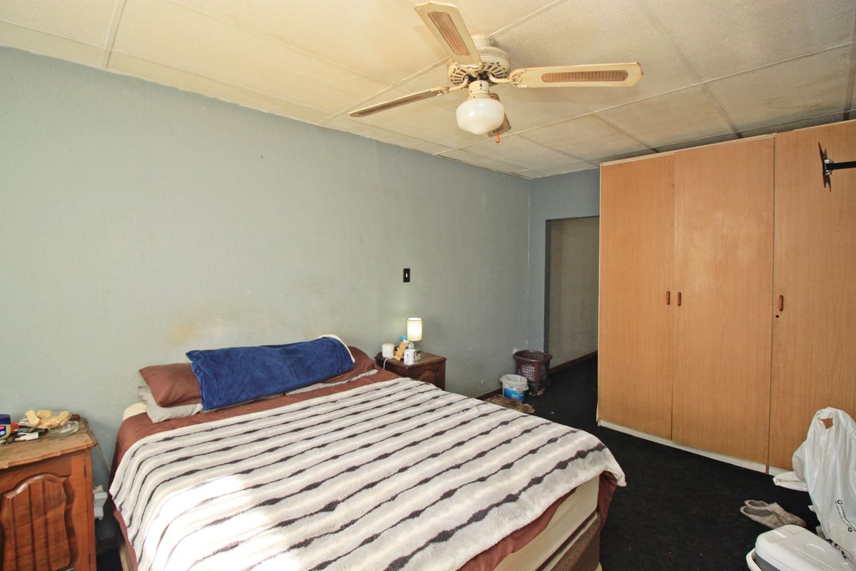 A bedroom featuring a ceiling fan, built-in wardrobe, and dark carpeting. The room requires cosmetic updates to improve its overall condition and appeal.