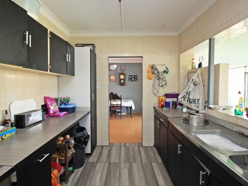 A functional galley-style kitchen featuring dark cabinetry, laminate countertops, a stainless steel sink, and tiled finishes throughout.