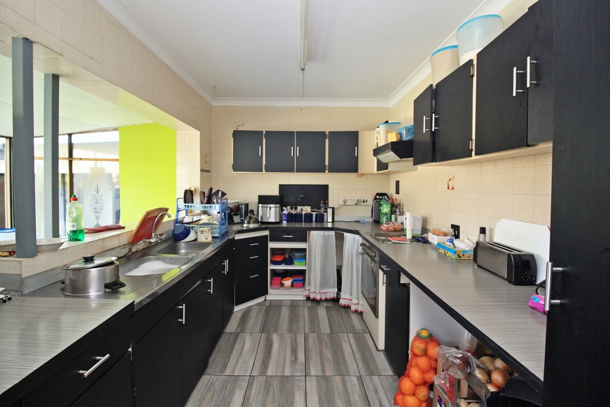 A functional kitchen featuring dark cabinetry, laminate countertops, a built-in oven, and tiled flooring, offering potential for a modern renovation.