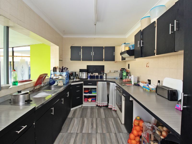 A functional kitchen featuring dark cabinetry, laminate countertops, a built-in oven, and tiled flooring, offering potential for a modern renovation.