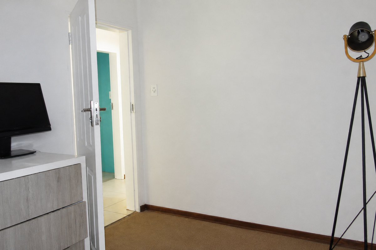 A bedroom interior featuring carpeted flooring, neutral walls, and an open doorway leading to an adjacent room.