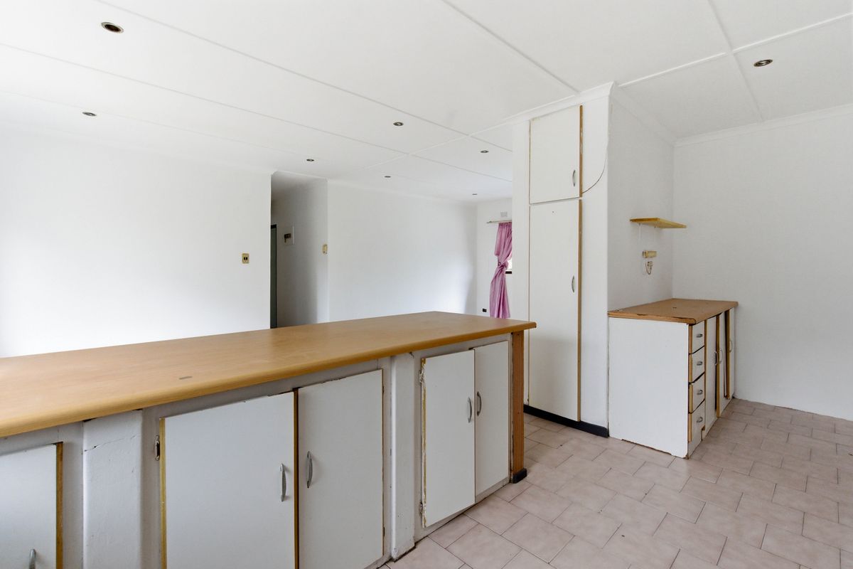 An empty kitchen space featuring built-in cabinetry, laminate countertops, and tiled flooring, offering a blank canvas for potential renovation and modernization.