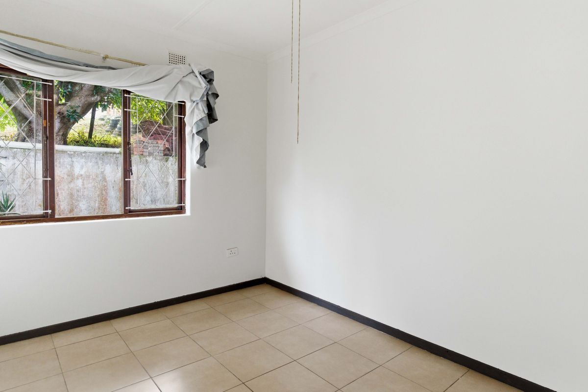 A vacant bedroom featuring neutral tiled flooring, white walls, and a window fitted with security burglar bars.