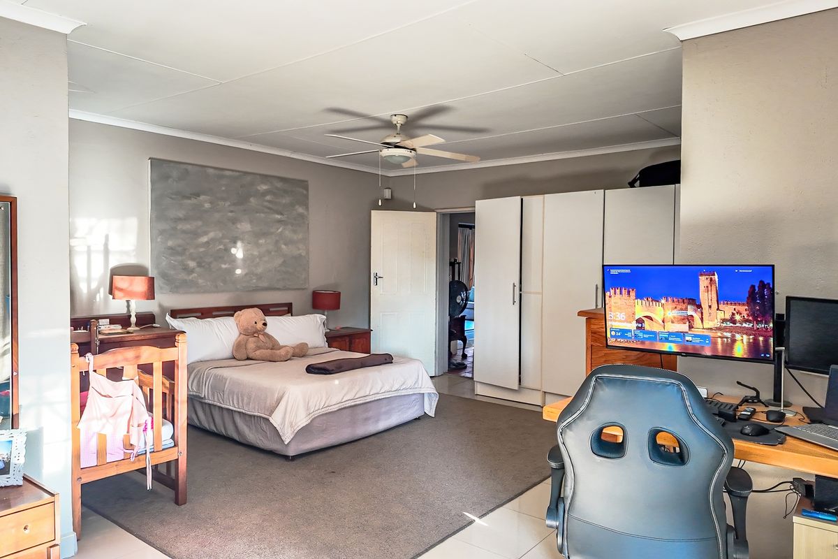 Spacious bedroom featuring built-in wardrobes, a ceiling fan, and neutral wall finishes, offering a functional layout with direct access to an adjoining room.