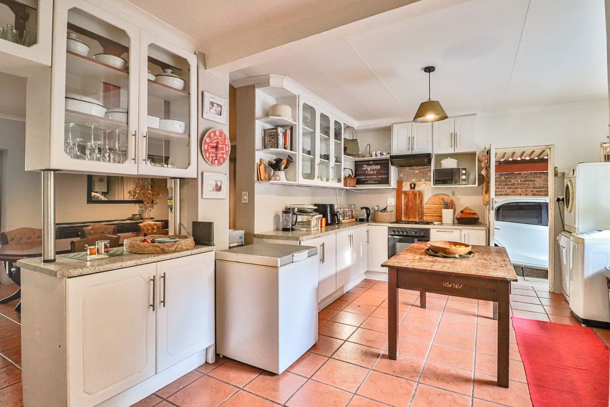 A functional kitchen featuring white cabinetry, stone-look countertops, and terracotta floor tiles, with an open layout connecting to adjacent living spaces.
