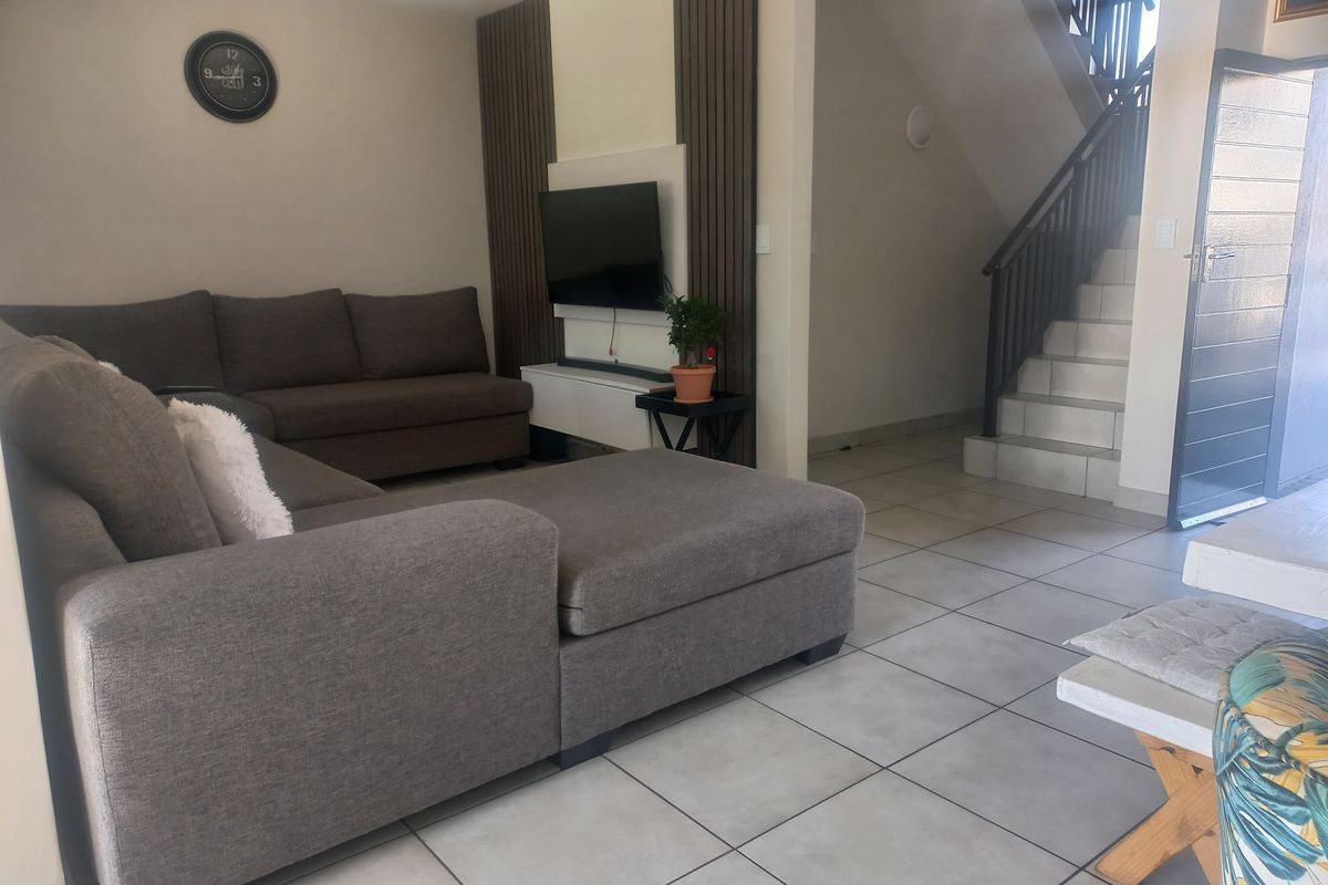 A well-maintained living room featuring tiled flooring, decorative wall paneling, and an integrated staircase with a modern metal railing.