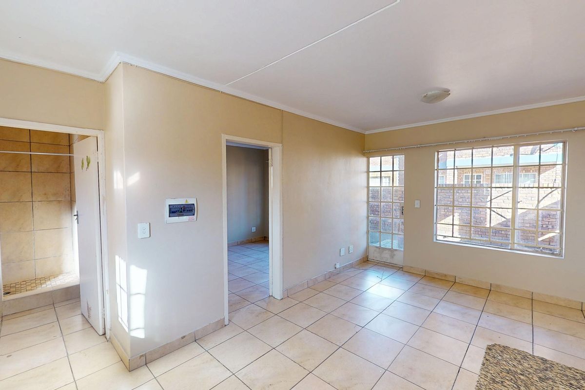 An empty living area featuring tiled flooring, neutral walls, and direct access to an adjacent room and exterior space.