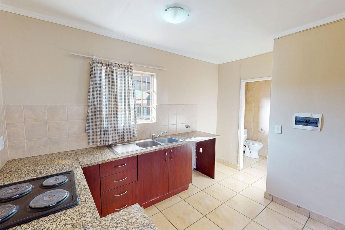 A functional kitchen featuring granite countertops, built-in cabinetry, an electric hob, and tiled flooring, with an adjacent view into a bathroom.