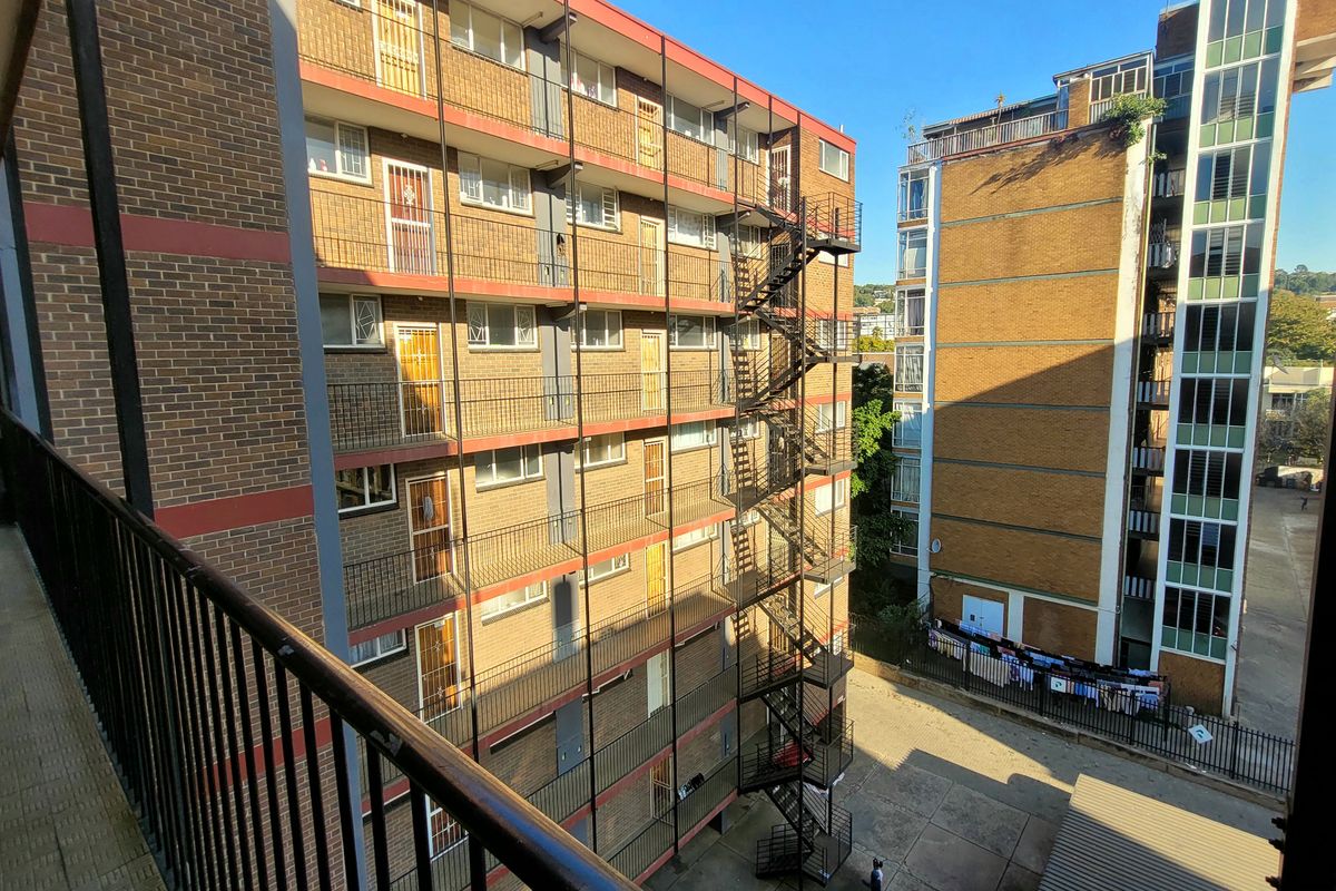 View of the apartment building exterior featuring brick facade, metal fire escape staircase, and a paved courtyard area.