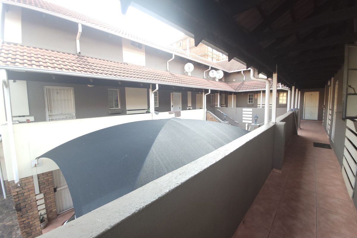 An elevated view of a residential complex walkway featuring tiled flooring, covered access, and a shade sail over the parking area.
