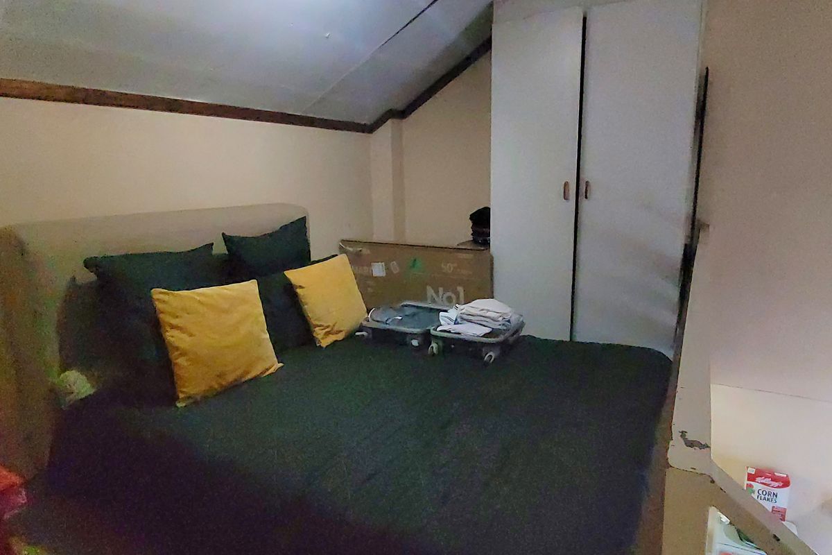 A compact bedroom featuring a sloped ceiling and a built-in wardrobe, offering a functional space with potential for cosmetic updates.