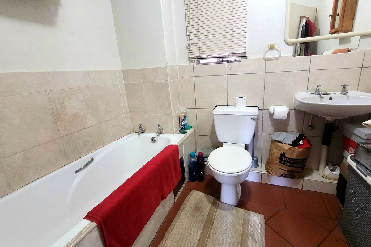 A functional bathroom featuring a bathtub, pedestal washbasin, and toilet with neutral wall tiling and terracotta floor tiles.