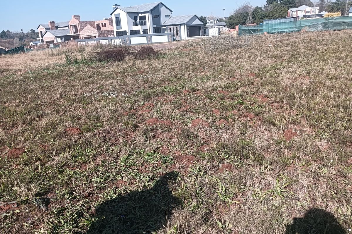 A vacant residential plot of land featuring natural grass coverage, situated in a developed neighborhood with surrounding residential properties.