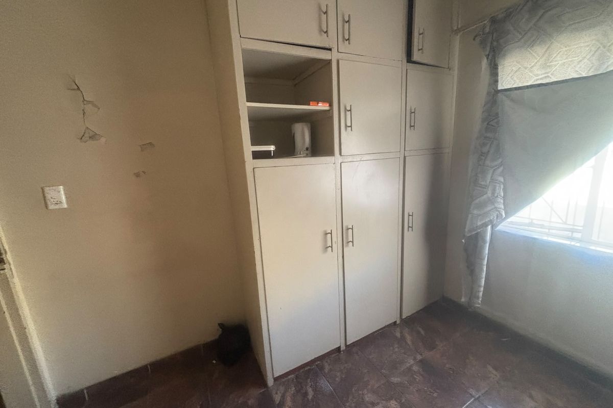 A bedroom featuring built-in storage cupboards and tiled flooring, requiring cosmetic updates to the wall finishes.