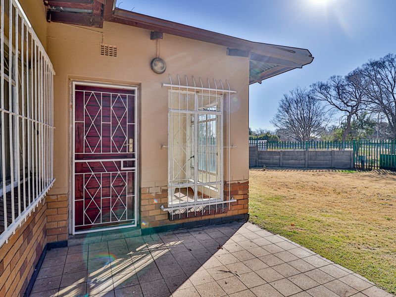 Rear exterior view featuring a tiled patio, security-fitted door and windows, and a spacious backyard with a perimeter boundary wall.